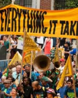 Protest sign reading "To change everything, it takes everyone"