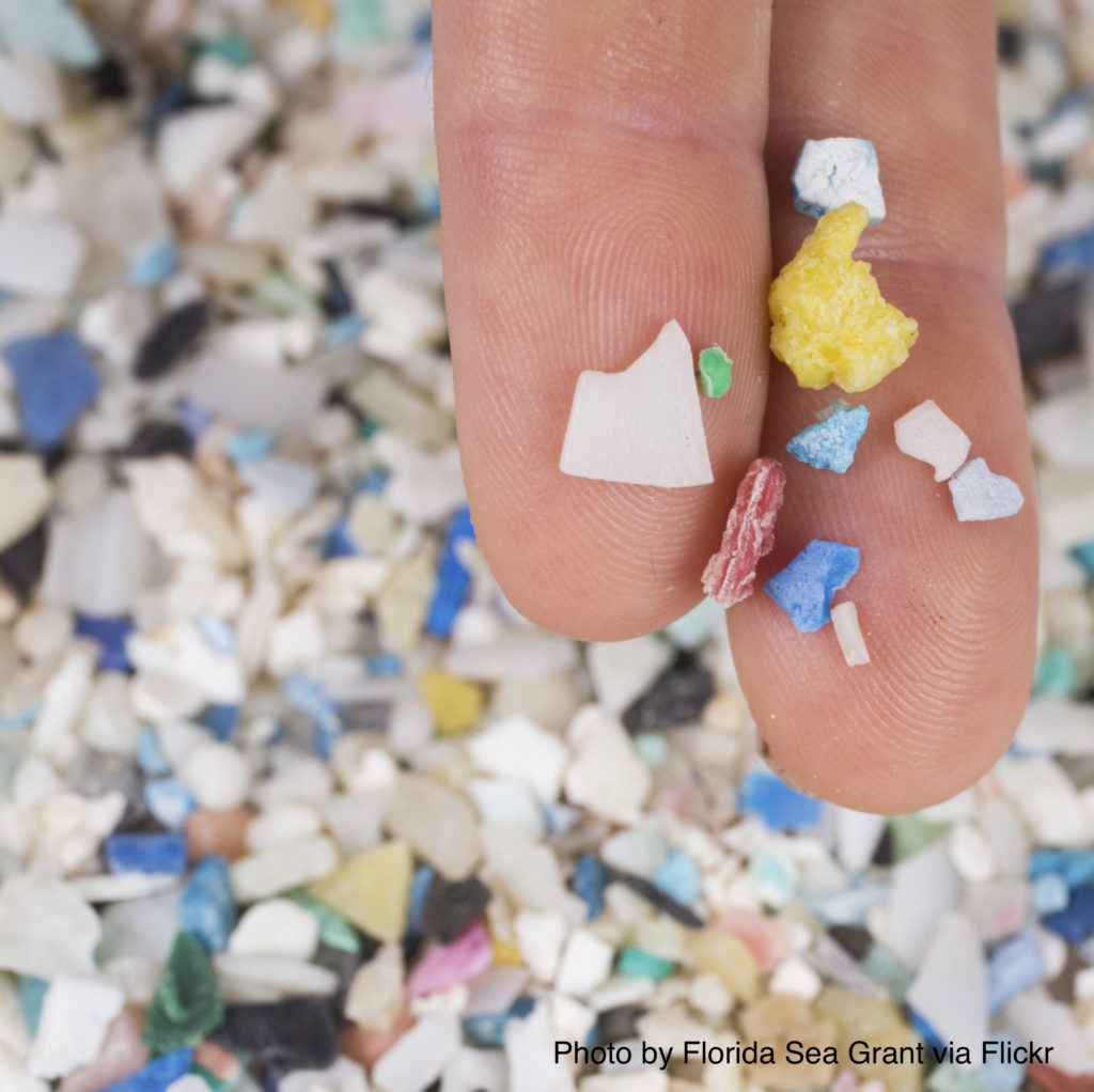A person holds plastic particles on their fingers. In the background is a pile of similar particles.