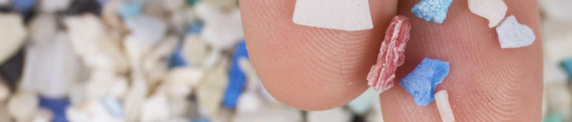 A person holds plastic particles on their fingers. In the background is a pile of similar particles.