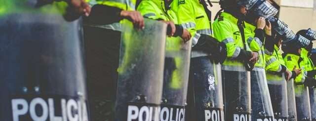 Police officers lined in a row wearing shields and masks.