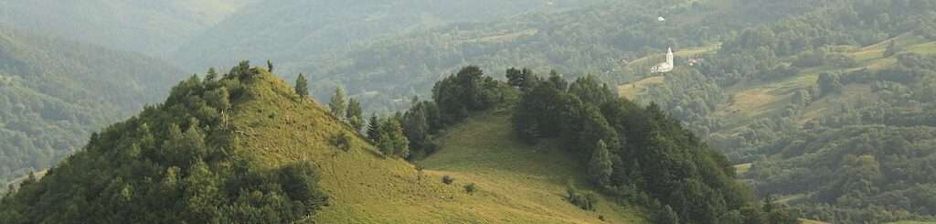 Rolling, green hills with a small, white building in the distance.