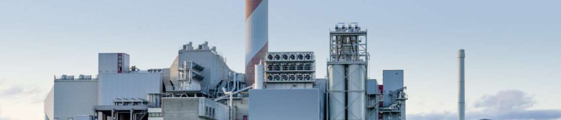 red and grey striped smoke stack in front of a grey industrial facility