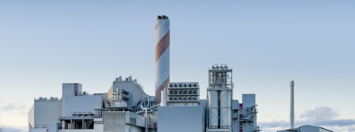 red and grey striped smoke stack in front of a grey industrial facility