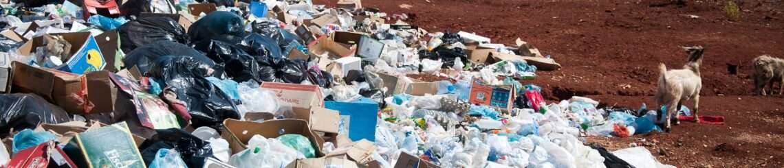 large pile of trash on a dirt, a waterway is in the distant background