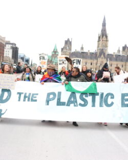 group of Indigenous leaders holding a banner that reads "End the plastic era" at a protest.