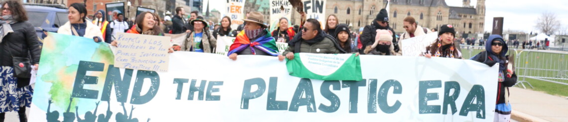 group of Indigenous leaders holding a banner that reads "End the plastic era" at a protest.