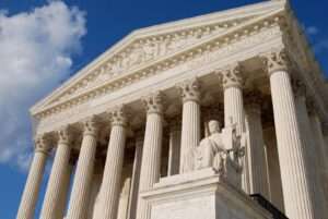 US Supreme Court Building a grand, neoclassical structure with a wide staircase leading up to a row of tall, imposing columns. Above the entrance, the words "Equal Justice Under Law" are inscribed.